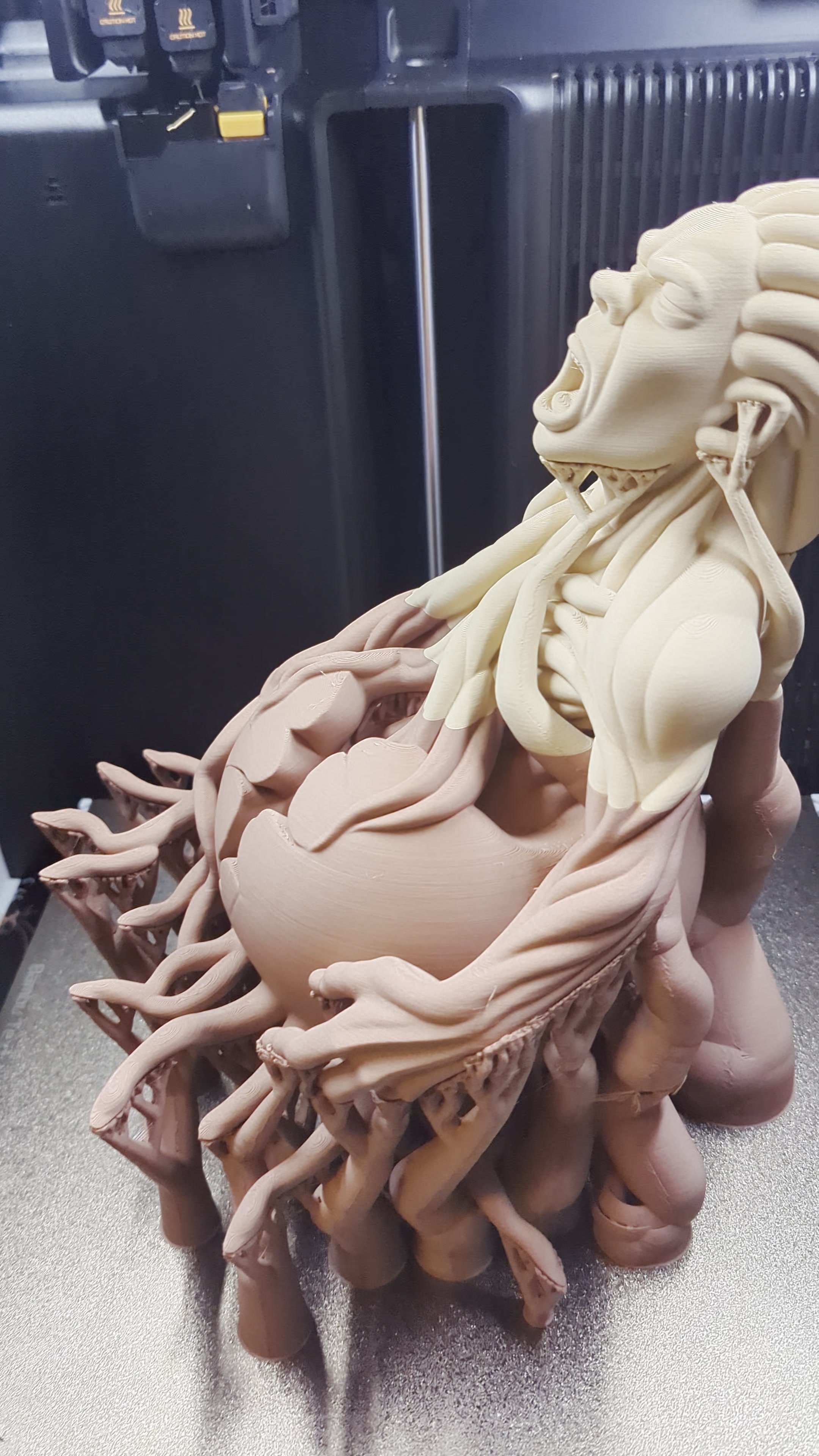 A large multicolor 3D-printed character sculpture beside a fabrication machine.